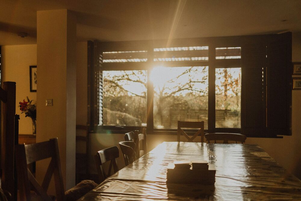 Table de salle à manger en bois baignée d'une lumière dorée, une pile de documents posée dessus, chaises vides autour