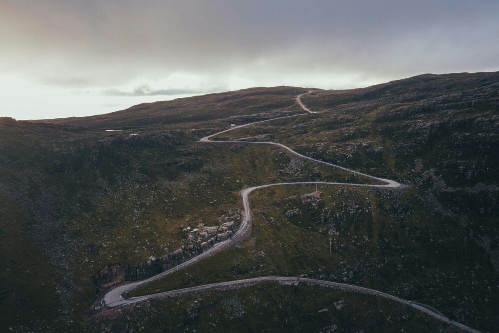 Route sinueuse vue d'en haut serpentant dans des hauts plateaux rocheux sous un ciel couvert
