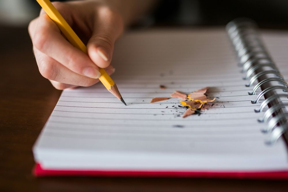 Main qui écrit au crayon dans un carnet à spirale ouvert