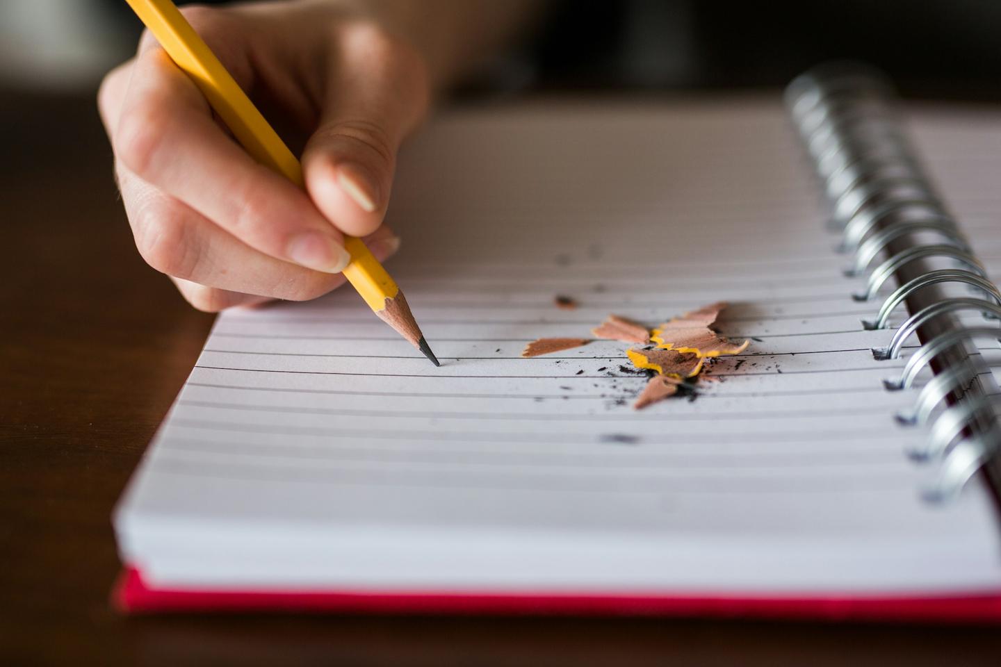Main qui écrit au crayon dans un carnet à spirale, photo de Thought Catalog